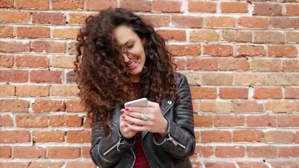 Портрет красивої молодої жінки зі смартфоном, що спирається на цегляну стіну, повільний рух — стокове відео