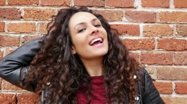 Bir tuğla duvarda güzel kıvırcık saçlı mutlu genç kadın Portresi, yavaş hareket