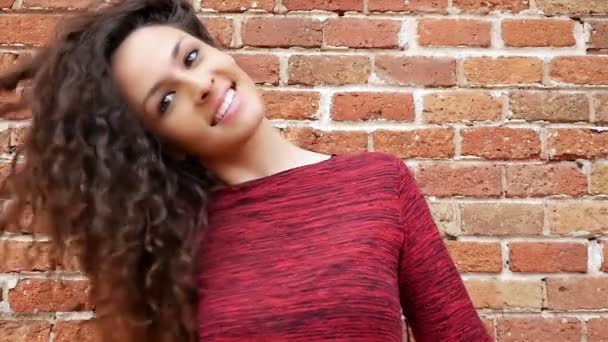 Portrait of happy young woman shaking her beautiful curly hair on brick wall, slow motion — Stock Video