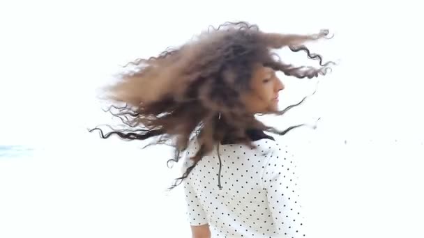 Νεαρή γυναίκα κουνάει τα όμορφα σγουρά μαλλιά της σε λευκό φόντο, αργή κίνηση — Αρχείο Βίντεο