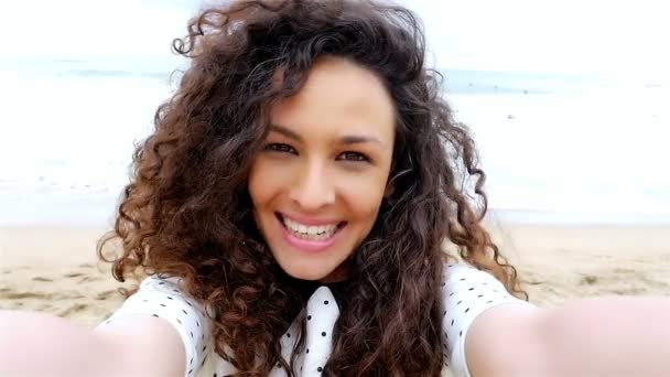 Портрет счастливой молодой женщины с красивыми вьющимися волосами, делающей селфи на пляже, замедленная съемка — стоковое видео