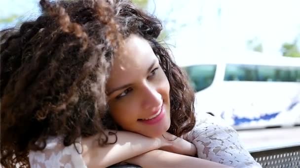 Портрет щасливої молодої жінки з красивим кучерявим волоссям, що спирається на голову на руки в місті, повільний рух — стокове відео