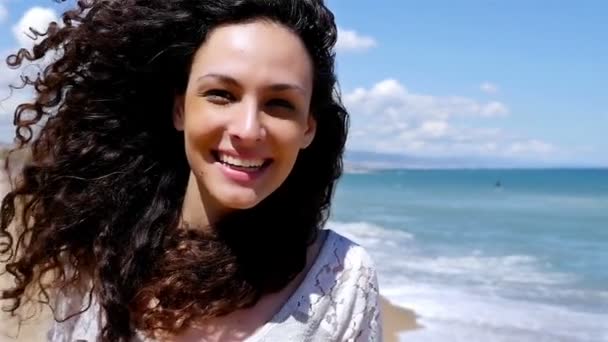 Портрет счастливой молодой женщины с красивыми вьющимися волосами на берегу моря, замедленная съемка — стоковое видео