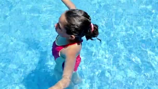 Маленька дівчинка в купальнику лежить на воді в басейні — стокове відео