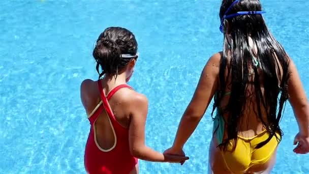 Две маленькие девочки в купальниках прыгают в бассейн, замедленная съемка — стоковое видео