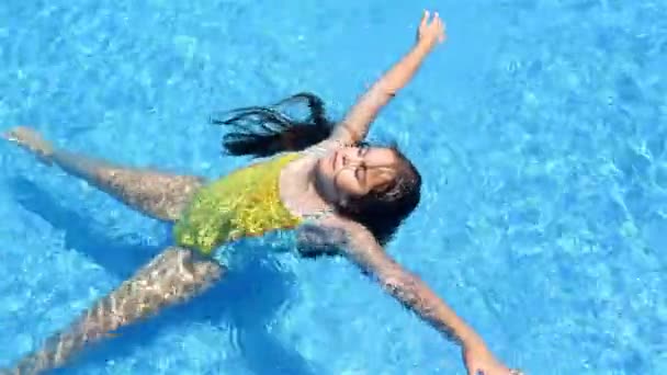 Niña en traje de baño acostada en el agua en la piscina — Vídeo de stock