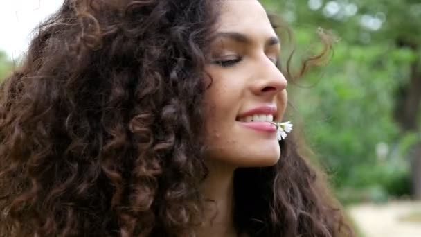Retrato de una hermosa joven con hermoso cabello rizado con una margarita en la boca, 4k — Vídeo de stock