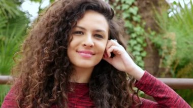 Güzel kıvırcık saçlı bir parkta gülümseyerek mutlu bir genç kadın portresi