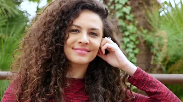 Портрет счастливой молодой женщины с красивыми вьющимися волосами, улыбающейся в парке — стоковое видео