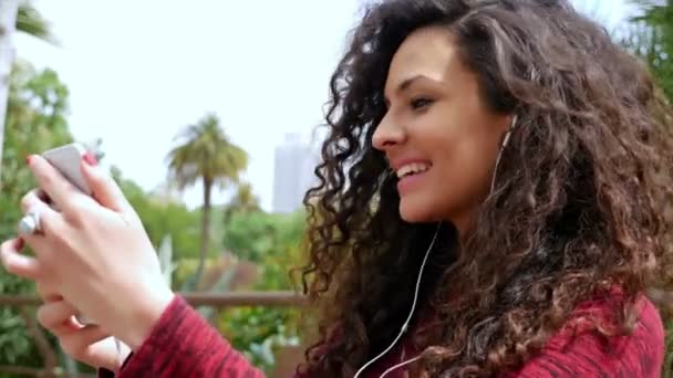 Junge Frau mit schönen lockigen Haaren, die im Park Musik hört — Stockvideo