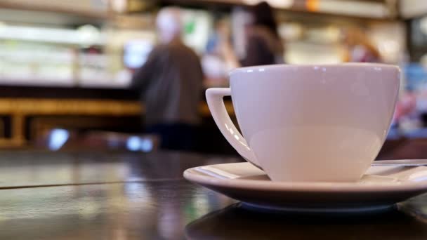 Personas desenfocadas en un café de interior, taza de café en frente — Vídeo de stock