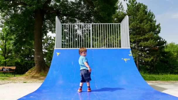 Malý kluk hraje na bruslení rampu na hřišti — Stock video