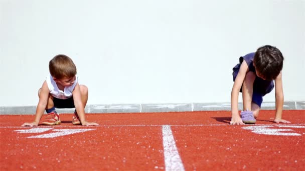 Vídeo divertido con dos niños pequeños preparándose para correr en una pista atlética — Vídeo de stock