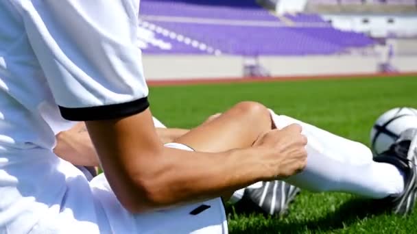 Voetballer in witte outfit aanpassen zijn sokken op het veld — Stockvideo