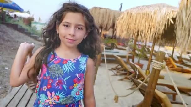 Linda niña caminando paraguas de paja y fondos marinos de madera en la playa — Vídeo de stock
