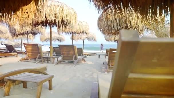 Schattig klein meisje amongstraw parasols en houten zeebodems draait op het strand — Stockvideo