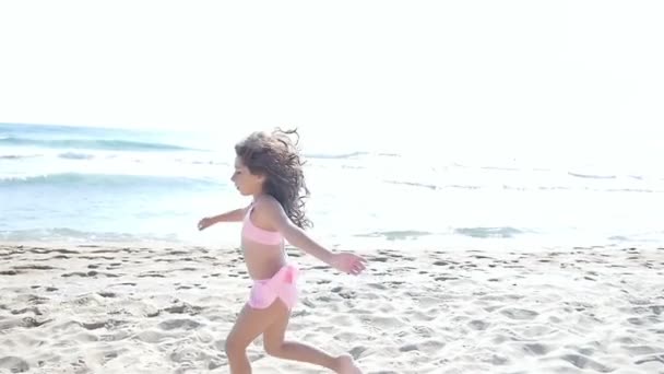 Cámara lenta de una linda niña en traje de baño corriendo y jugando en la playa del mar — Vídeos de Stock