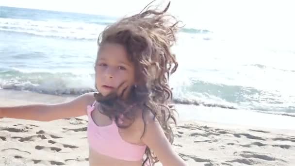 Cámara lenta de una linda niña en traje de baño corriendo y jugando en la playa del mar — Vídeos de Stock