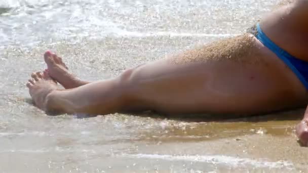 Woman relaxing on the beach, waves splashing in her body, legs only — Stock Video