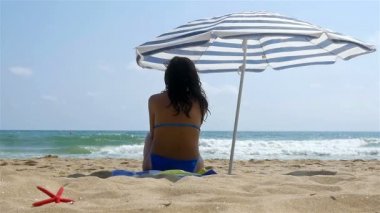Plajda şemsiye altında güneşlenme oturan kadın yavaş hareket