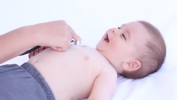 Kid médico examinando menino feliz com estetoscópio em um fundo branco — Vídeo de Stock