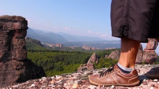 Los pies masculinos en zapatos deportivos pisan una roca, los turistas admiran el valle de Belogradchik — Vídeo de stock