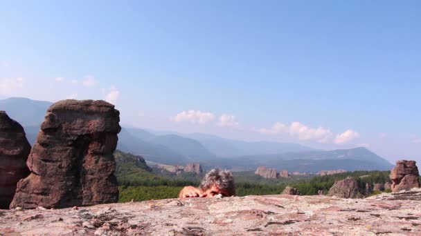 El hombre está escalando una roca y sentado para admirar el hermoso valle de Belogradchik — Vídeos de Stock