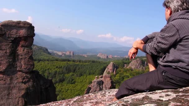 Kayanın üzerinde oturan ve güzel Belogradchik Vadisi hayran bir adam — Stok video