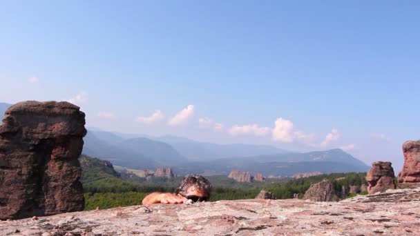 Man is een rots klimmen en zit te bewonderen van de prachtige vallei van Belogradchik — Stockvideo