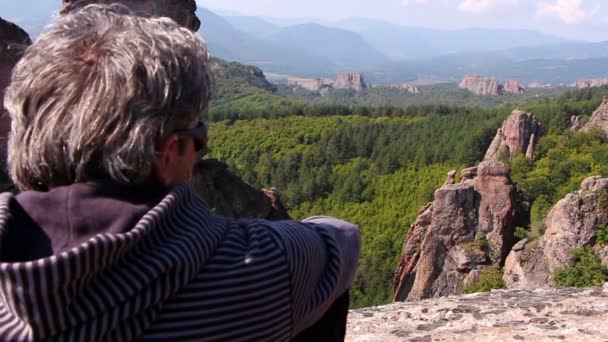 Kayanın üzerinde oturan ve güzel Belogradchik Vadisi hayran bir adam — Stok video