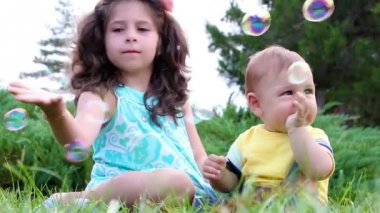 Sevimli kız ve onun küçük kardeşi sabun köpüğü ile eğleniyor çimenlerin üzerinde