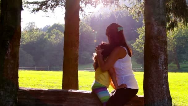Mother and daughter hugging and kissing on tree log. Sunset in the background — Stock Video