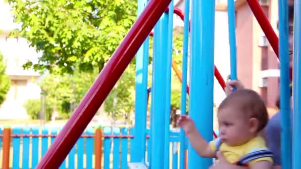Madre y su pequeño hijo se balancean en un patio de recreo — Vídeos de Stock