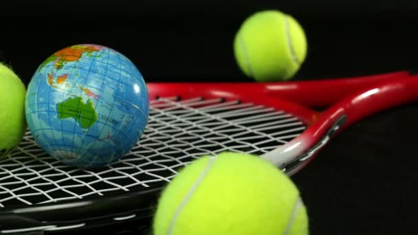 Теннисное оборудование - теннисная ракетка с тремя теннисными мячами и одним шаром земной шар на черном фоне, кукла — стоковое видео