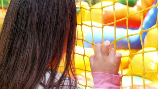 Ein Mädchen beobachtet Kinder, die auf einem aufblasbaren Gummiburg-Spielplatz spielen. Erholung im Freien für Kinder — Stockvideo