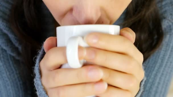 Woman in warm vest sipping her hot drink / coffee / tea, camera close up in front of model — ストック動画