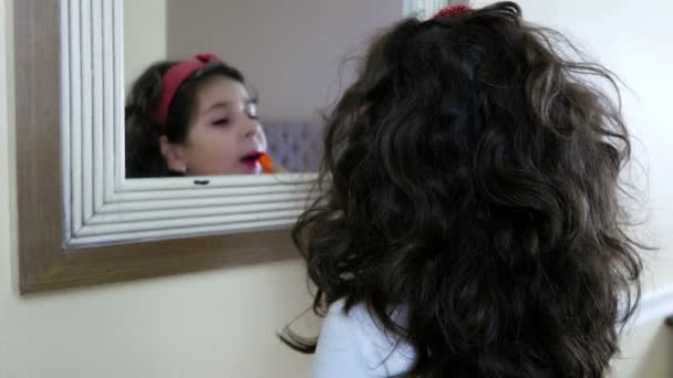 Schönes kleines Mädchen, das einen Lippenstift vor den Spiegel hält und in die Kamera lächelt — Stockvideo