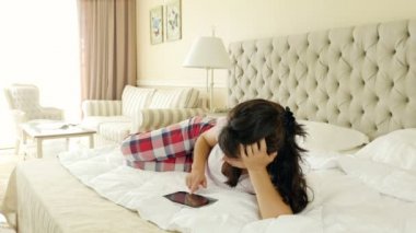 Yatakta yatan kadın tablet bilgisayar dokunmatik evde, kullanarak bir pijama