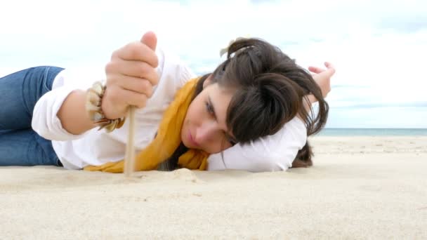 Lachende vrouw liggend op het strand en spelen met het zand — Stockvideo