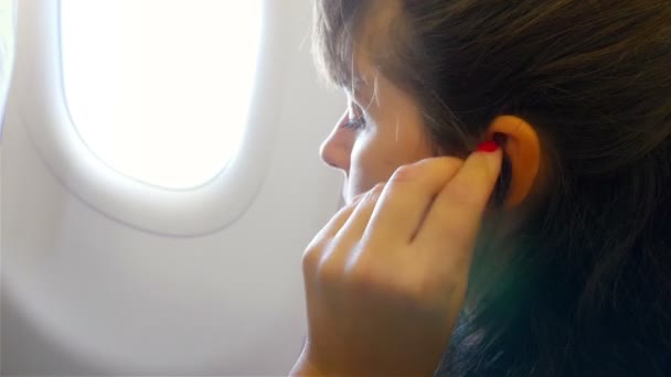 飛行機の窓のそばに座っている女性は彼のヘッドフォンを置きます。自分のコンテンツを配置するためのスマートフォンのクロマキー画面. — ストック動画