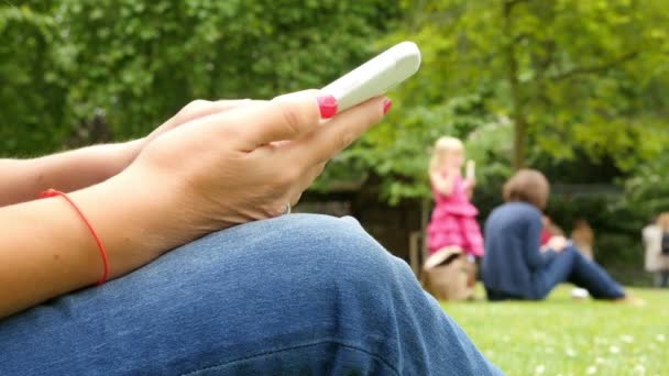 Primo piano della donna che utilizza il telefono cellulare seduto in un parco, solo le mani — Video Stock