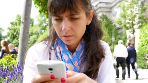 Mujer usando un teléfono inteligente mientras está sentada en un parque en Londres — Vídeo de stock