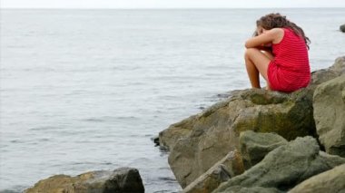 Deniz kıyısında buzlu ayakta ve denize bakarak kırmızı yazlık elbise, küçük kız
