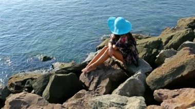 Yazlık elbise ve mavi şapka buzlu deniz kıyısında oturan genç kadın