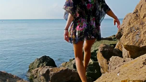 Jovem mulher em vestido de verão e chapéu azul sentado em rochas na costa do mar — Vídeo de Stock