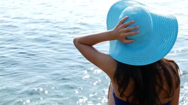 Young woman in swimming suit and blue hat sitting on rocks on the sea shore — Stock Video