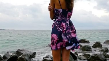 Yazlık elbise, eşarp ve günbatımı, deniz dalgaları kaza buzlu denizde tarafından kayalık sahil üzerinde şapka duran genç kadınla