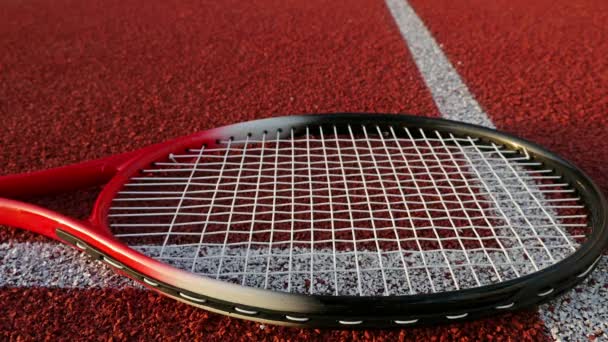 Raquete de tênis deitado no campo de ténis vermelho, mão coloca três bolas de tênis sobre ele — Vídeo de Stock