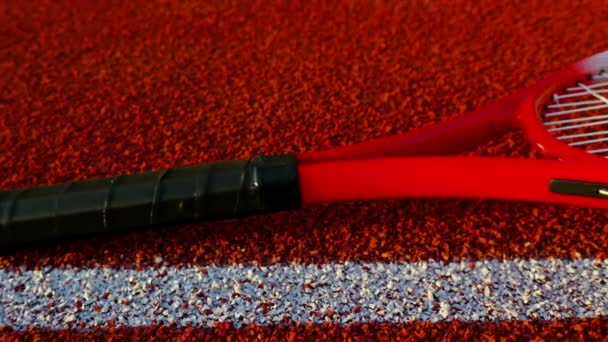 Raqueta de tenis y tres pelotas tendidas en pista de tenis roja, muñeca — Vídeo de stock