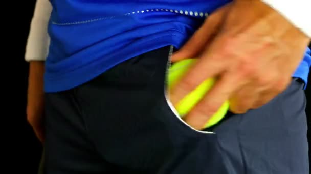 Теннисист кладет теннисный мяч в карман и готовится к подаче, черный фон — стоковое видео